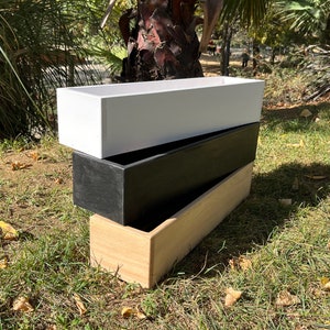 May include: Three wooden planter boxes stacked on top of each other. The top box is white, the middle box is black, and the bottom box is natural wood.