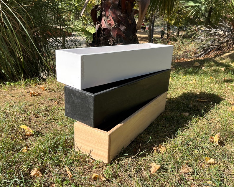 May include: Three wooden planter boxes stacked on top of each other. The top box is white, the middle box is black, and the bottom box is natural wood.