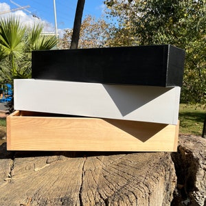 May include: Three wooden boxes stacked on top of each other. The top box is black, the middle box is white, and the bottom box is natural wood.