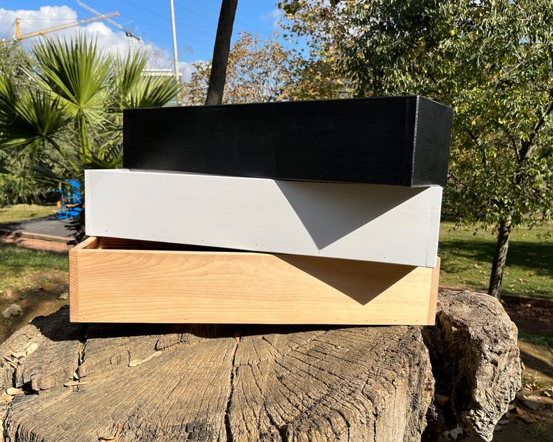 May include: Three wooden boxes stacked on top of each other. The top box is black, the middle box is white, and the bottom box is natural wood.