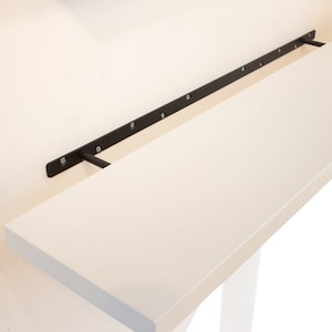 May include: A white shelf with black metal brackets attached to a white wall. The shelf is mounted to the wall with screws.