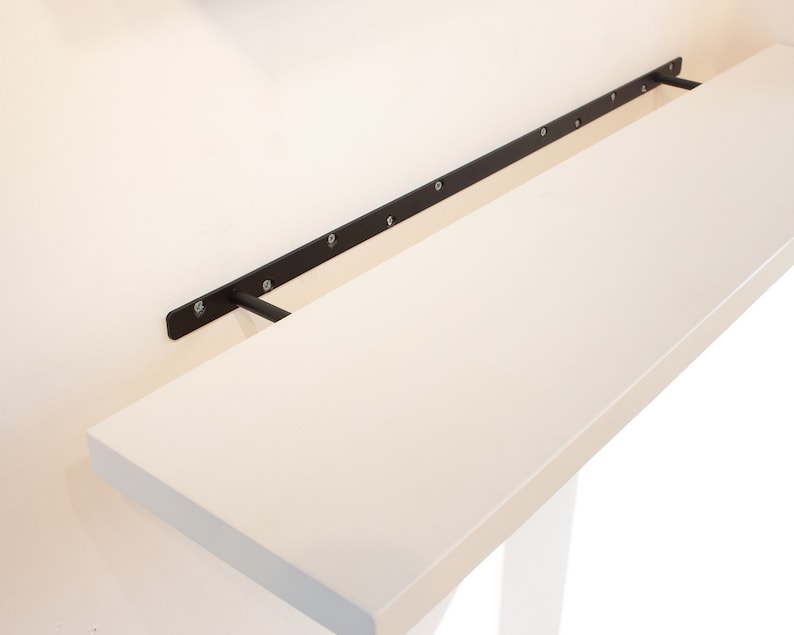May include: A white shelf with black metal brackets attached to a white wall. The shelf is mounted to the wall with screws.
