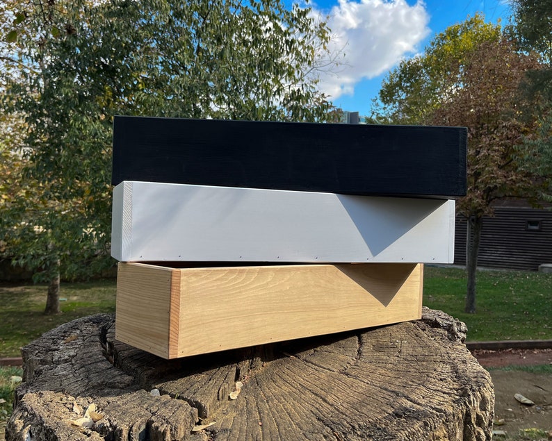 May include: Three wooden boxes stacked on top of each other. The top box is black, the middle box is white, and the bottom box is natural wood.