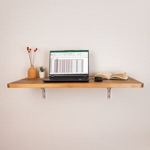 Puede incluir: Una estanter&iacute;a de madera con un ordenador port&aacute;til, un libro y un rat&oacute;n. El port&aacute;til est&aacute; abierto y muestra una hoja de c&aacute;lculo con datos. La estanter&iacute;a est&aacute; montada en una pared blanca.