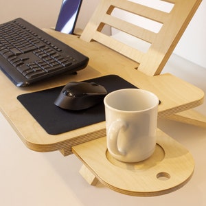 May include: A wooden laptop stand with a built-in keyboard tray, mouse pad, and cup holder. The stand is made of light wood and has a natural finish.