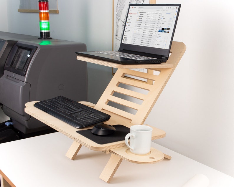 May include: A wooden laptop stand with a keyboard, mouse, and a white mug on a shelf. The stand is adjustable to different heights and angles.
