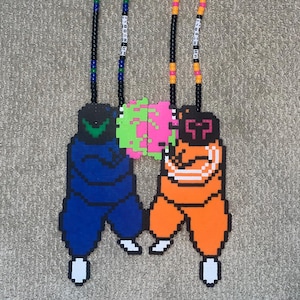 May include: Two beaded necklaces with pixelated pendant designs. One pendant is blue with a green head, the other is orange with a black head. The pendants appear to be hugging a green and pink sphere. The necklaces have black beads with colorful accents.
