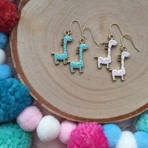 Op de afbeelding: Een paar gouden oorbellen met een giraffenontwerp. Het ene paar is turquoise blauw en het andere is wit.