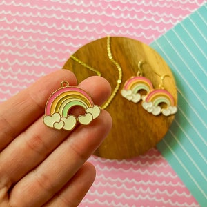 May include: A gold-tone rainbow pendant necklace and matching earrings with white clouds and hearts. The rainbow is multi-coloured with pink, yellow, and green stripes.