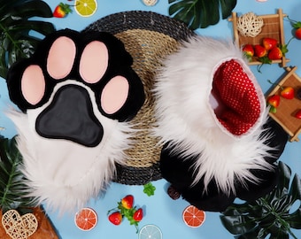 May include: A pair of black and white furry paw hand warmers with pink paw pads. The hand warmers are on a blue background with fruit and leaves.