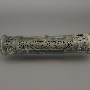 May include: A cylindrical metal incense burner featuring an intricate openwork pattern of scrolling vines and floral motifs. The dark, weathered surface displays a matte finish with visible signs of age, including a small central latch.