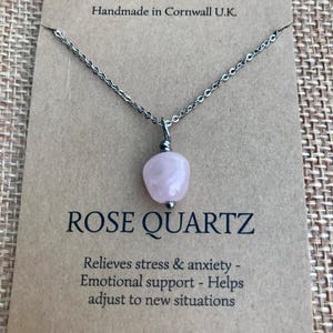 Pode incluir: Um colar com pingente de quartzo rosa e corrente prateada. O pingente &eacute; uma pedra rosa claro polida. O colar &eacute; exibido em um cart&atilde;o marrom com o texto "CALMER & KARMA" e "ROSE QUARTZ". O cart&atilde;o tamb&eacute;m diz "Handmade in Cornwall U.K."