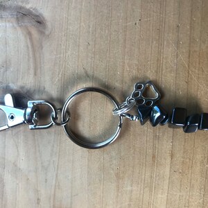 May include: A silver key chain with a black hematite stone charm and a silver paw print charm.