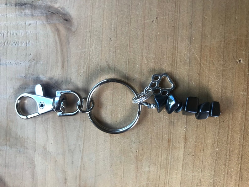 May include: A silver key chain with a black hematite stone charm and a silver paw print charm.