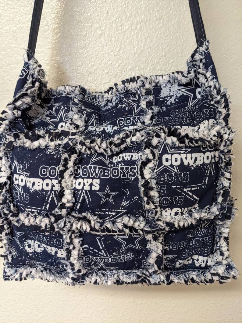 May include: A blue and white patchwork tote bag with a frayed edge. The bag is decorated with a repeated pattern of the Dallas Cowboys logo and the words "Cowboys" and "Go Cowboys".
