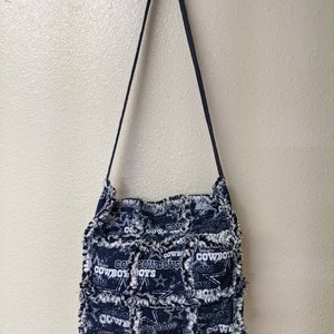 May include: A black and white patchwork tote bag with a frayed edge. The bag features a repeated pattern of the Dallas Cowboys logo and the words "Go Cowboys".
