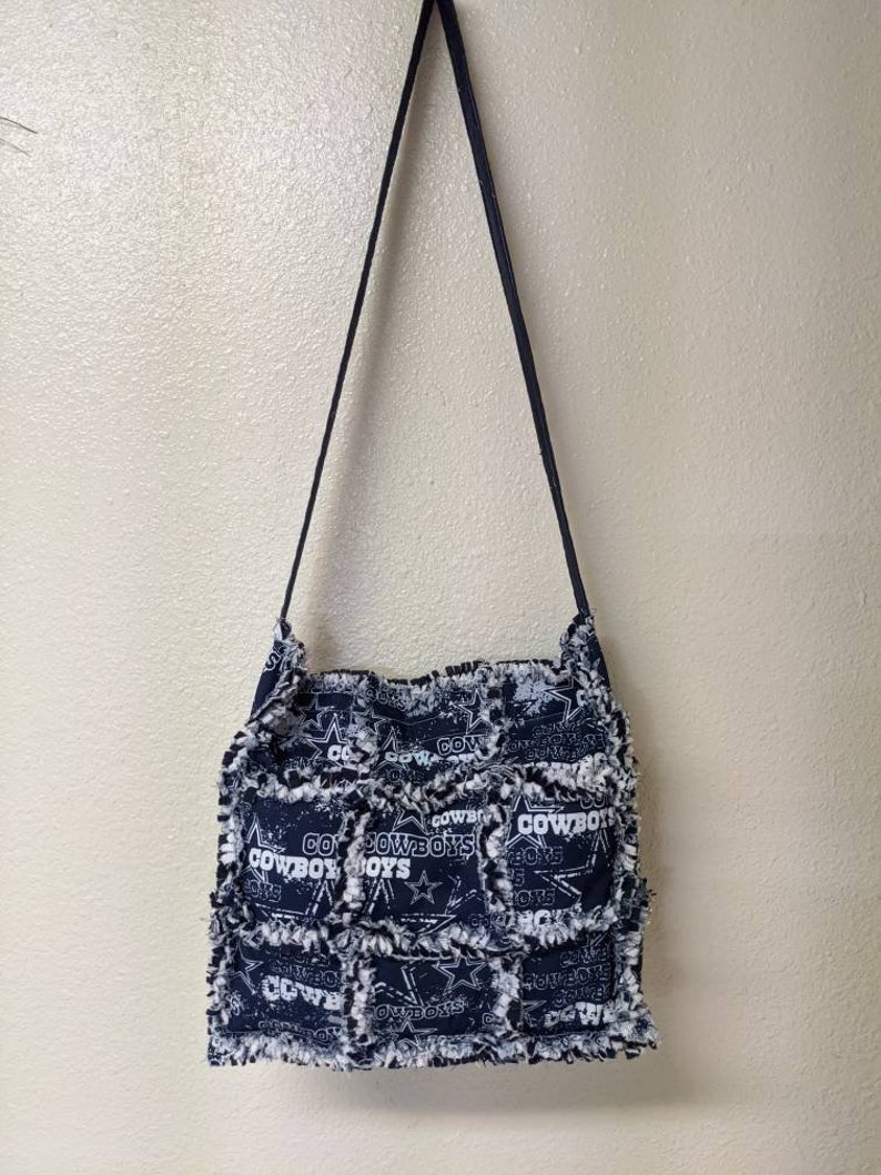 May include: A black and white patchwork tote bag with a frayed edge. The bag features a repeated pattern of the Dallas Cowboys logo and the words "Go Cowboys".