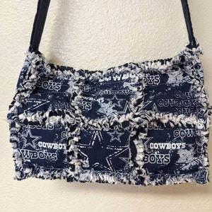 May include: A blue and white patchwork tote bag with a frayed edge. The bag features a repeated pattern of stars and the words "Cowboys" and "Boys".