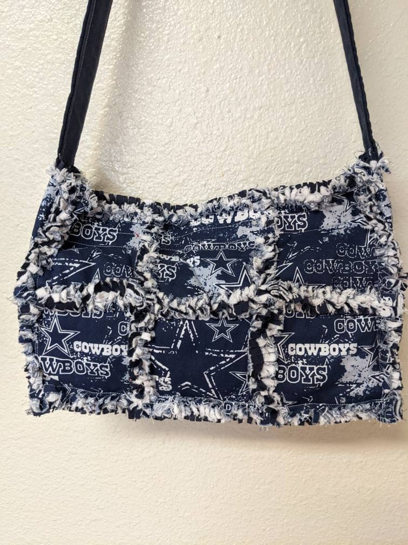 May include: A blue and white patchwork tote bag with a frayed edge. The bag features a repeated pattern of stars and the words "Cowboys" and "Boys".