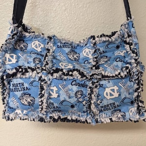 May include: A blue and white patchwork tote bag with a frayed edge. The bag features the University of North Carolina Tar Heels logo and the words "North Carolina" and "Tar Heels".