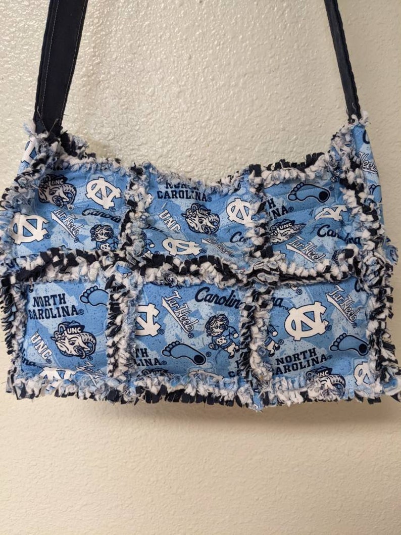 May include: A blue and white patchwork tote bag with a frayed edge. The bag features the University of North Carolina Tar Heels logo and the words "North Carolina" and "Tar Heels".