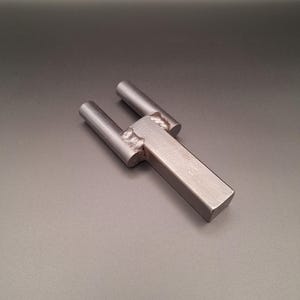 May include: A silver metal tool with two prongs and a rectangular handle. The tool is designed for use in metalworking or crafting.