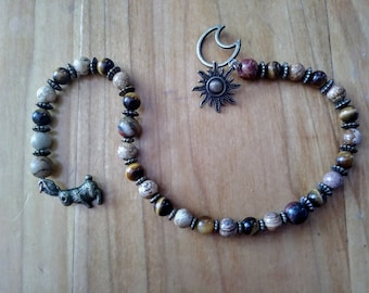 May include: A beaded strand featuring round tiger eye and jasper stones in shades of brown, tan, and gold, accented with small silver-toned metal spacers. The strand includes a silver-toned sun and moon charm at one end and a small rabbit charm at the other.
