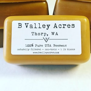 May include: A rectangular block of golden-yellow beeswax with a white label. The label reads "B Valley Acres, Thorp, WA" and states the product is 100% pure USA beeswax, naturally filtered, non-toxic, and in 1 lb blocks. The website is www.bvalleyacres.com.