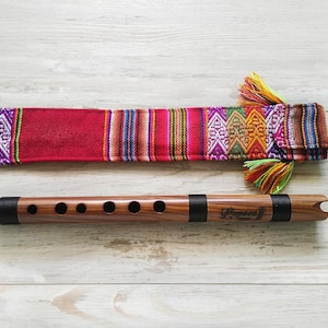 May include: A wooden flute with six holes and a black band. The flute is in a colorful woven fabric case with tassels.