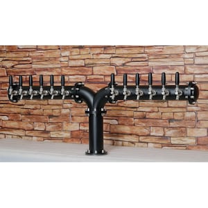 Könnte beinhalten: Ein schwarzer Bierzapfhahn aus Metall mit 12 Zapfhähnen. Der Turm hat eine Y-Form und einen schwarzen Sockel. Der Turm ist an einer Backsteinwand montiert.