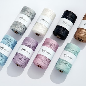 May include: Eight spools of macrame cord arranged in two rows, featuring colors including silver, white, black, bronze, light blue, lavender, pink, and mint green. Each spool has a white paper label with the text SHEweave printed in black.