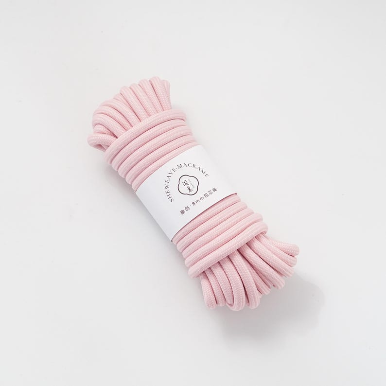 May include: A bundle of light pink macrame cord with a white label wrapped around it. The label has the text "SHEWEAVE-MACRAME" and other text in a different language. The cord is 8mm thick.