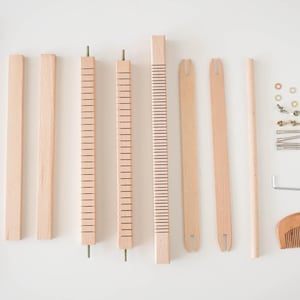 May include: A disassembled wooden weaving loom kit, featuring various components like frame pieces, rods, a comb, and hardware. The natural wood color of the parts creates a neutral palette, ideal for craft projects.