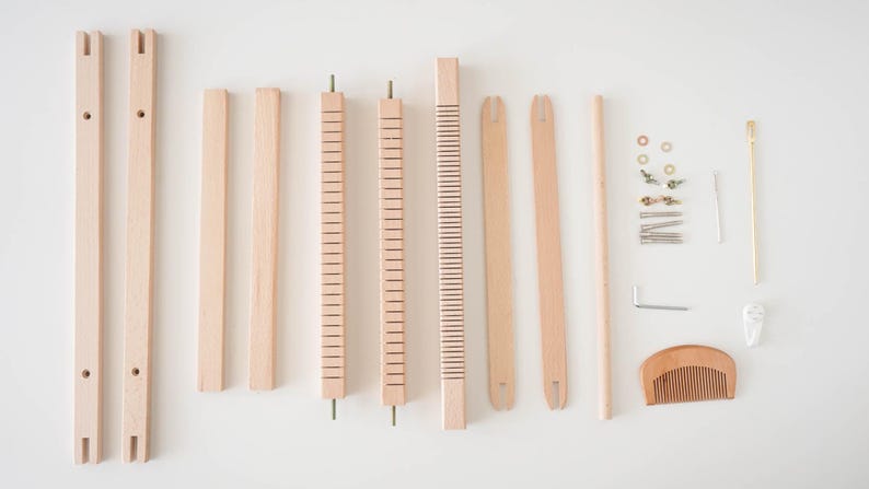 May include: A disassembled wooden weaving loom kit, featuring various components like frame pieces, rods, a comb, and hardware. The natural wood color of the parts creates a neutral palette, ideal for craft projects.