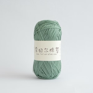 May include: A ball of pale green yarn with a cream-colored label wrapped around it. The label features Chinese characters and the English text "xue fei er mian cao". The yarn is tightly wound and appears to be made of a textured material.