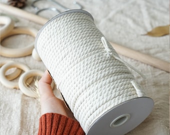 Könnte beinhalten: Eine Rolle aus cremefarbener, dicht gewebter Baumwollschnur. Das Seil ist um einen grauen Pappkern gewickelt. Das Bild zeigt eine Nahaufnahme des Seils, die seine Textur und die Art und Weise, wie es aufgerollt ist, hervorhebt. Das Seil eignet sich für verschiedene Bastelprojekte.
