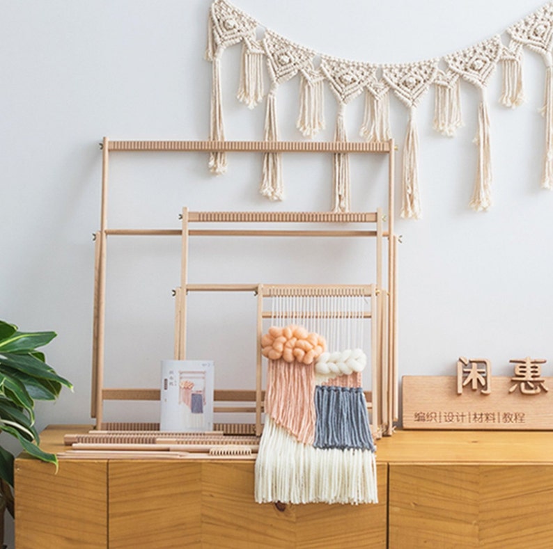 May include: A wooden weaving loom set with a partially completed woven wall hanging in peach, white, and blue. A macrame wall hanging is displayed above the loom. A small book and a wooden sign with Chinese characters are also visible.