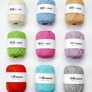 May include: Nine skeins of yarn in various colors, including cream, blue, tan, green, pink, purple, red, turquoise, and gray. Each skein has a white label with the text "SHEweave" and Chinese characters. The yarn is tightly wound and ready for crafting.