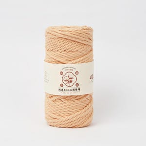 May include: A cylindrical spool of peach-colored cotton cord wrapped in a paper band. The band features a central circular logo with a cotton plant illustration, the text "4mm", and Chinese characters. The cord has a thick, twisted texture.