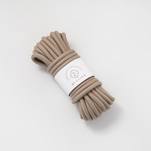 May include: A bundle of beige macrame cord, tightly wound and secured with a white label. The label features the text "SHEAVE MACRAME" and additional text in a different language. The cord appears to be approximately 8mm in diameter.