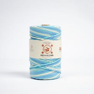 May include: A spool of blue, light blue, and white cotton yarn. The yarn is wrapped around a cardboard core and has a label with Chinese text and a cotton flower logo. The spool is approximately 30 meters in length.