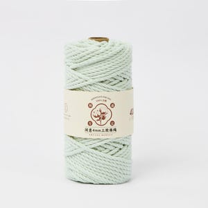 May include: A spool of light mint green cotton cord wrapped in a cylindrical shape. A beige paper label is wrapped around the center, featuring a brown graphic of a cotton plant, Chinese text, and the number 40, indicating a 4mm thickness.