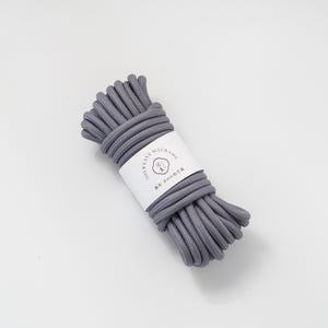 May include: A bundle of gray macrame cord with a white label wrapped around it. The label reads "SHEWEAVE MACRAME" and includes text in a different language. The cord appears to be 8mm in diameter.