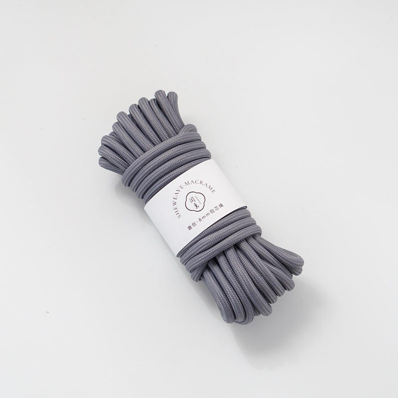 May include: A bundle of gray macrame cord with a white label wrapped around it. The label reads "SHEWEAVE MACRAME" and includes text in a different language. The cord appears to be 8mm in diameter.