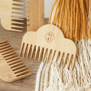 May include: A selection of bamboo combs with wide teeth and a natural finish. One comb has a cloud-like shape and the text "SHEWEAVE" with a logo. The background features a macrame wall hanging. The combs are made of bamboo.