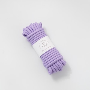 May include: A bundle of lavender macrame cord with a white label wrapped around it. The label reads "SHEWEAVE-MACRAME" and "8mm". The cord is tightly wound and ready for crafting projects. The background is a solid white.
