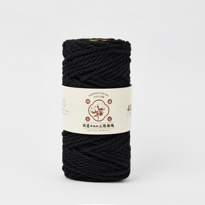 May include: A cylindrical spool of black cotton cord wrapped in a cream-colored paper label. The label features a central illustration of a cotton plant, Chinese text, and the specific measurement of 4mm printed clearly on the front surface.