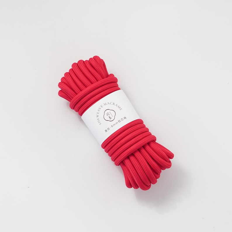 May include: A bundle of bright red macrame cord. The cord is tightly wound and wrapped with a white label that has black text and a circular logo. The cord appears to be approximately 8mm in diameter.