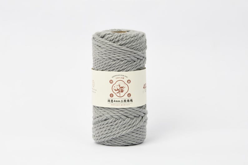 May include: A cylindrical spool of light gray twisted cotton cord wrapped in a paper band. The band features a central illustration of a cotton plant, the text "MADE JUST FOR YOU," and the Chinese characters "闲惠4mm三股棉绳" printed in brown.
