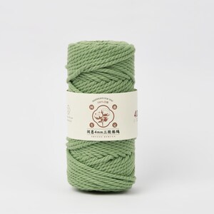 May include: A cylindrical spool of sage green cotton cord wrapped in a cream-colored paper band. The band features a central brown graphic of a cotton plant, Chinese characters, and the text 4mm, indicating the thickness of the twisted cord.